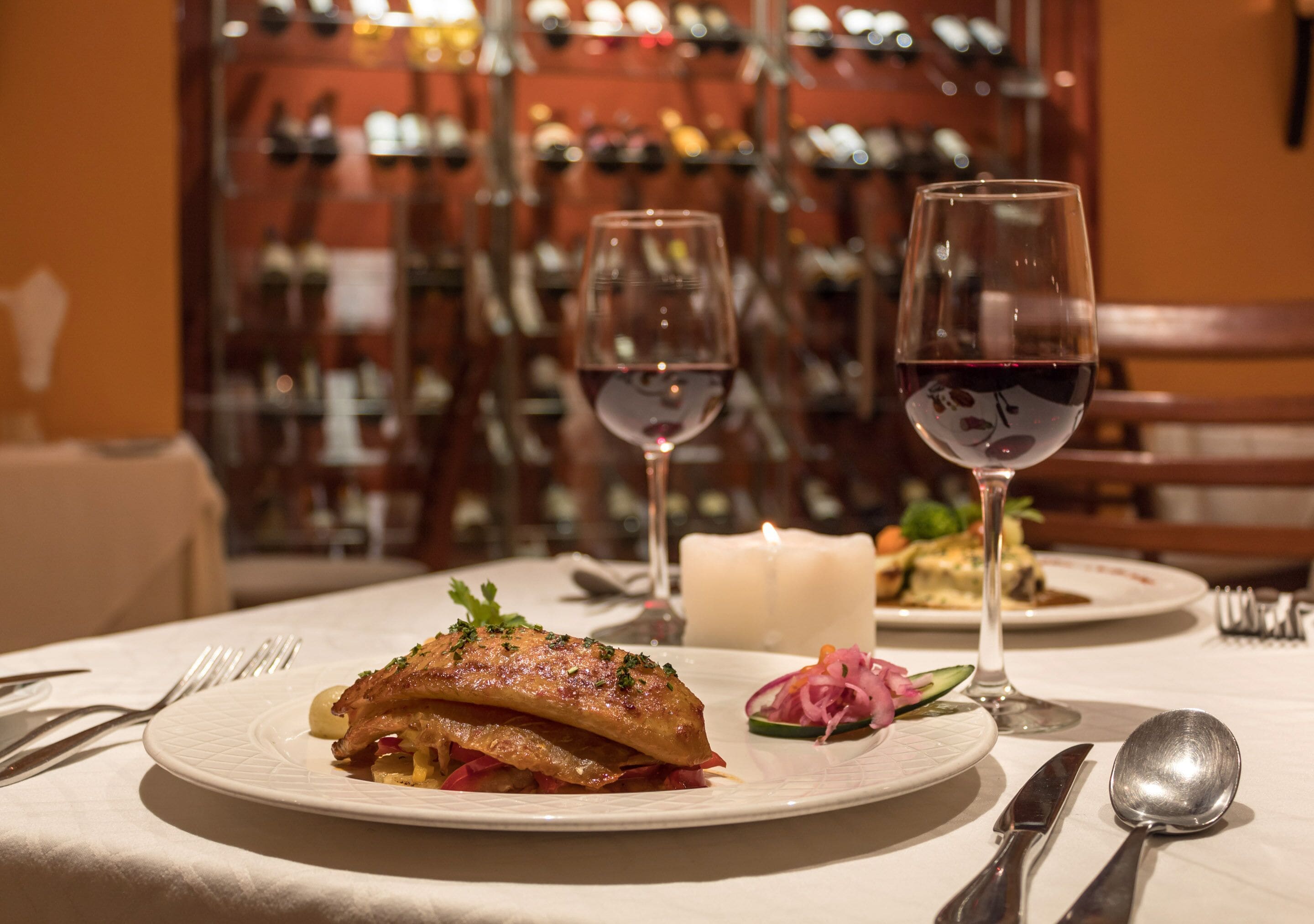 A dining table with plates of food, wine glasses, and cutlery.
