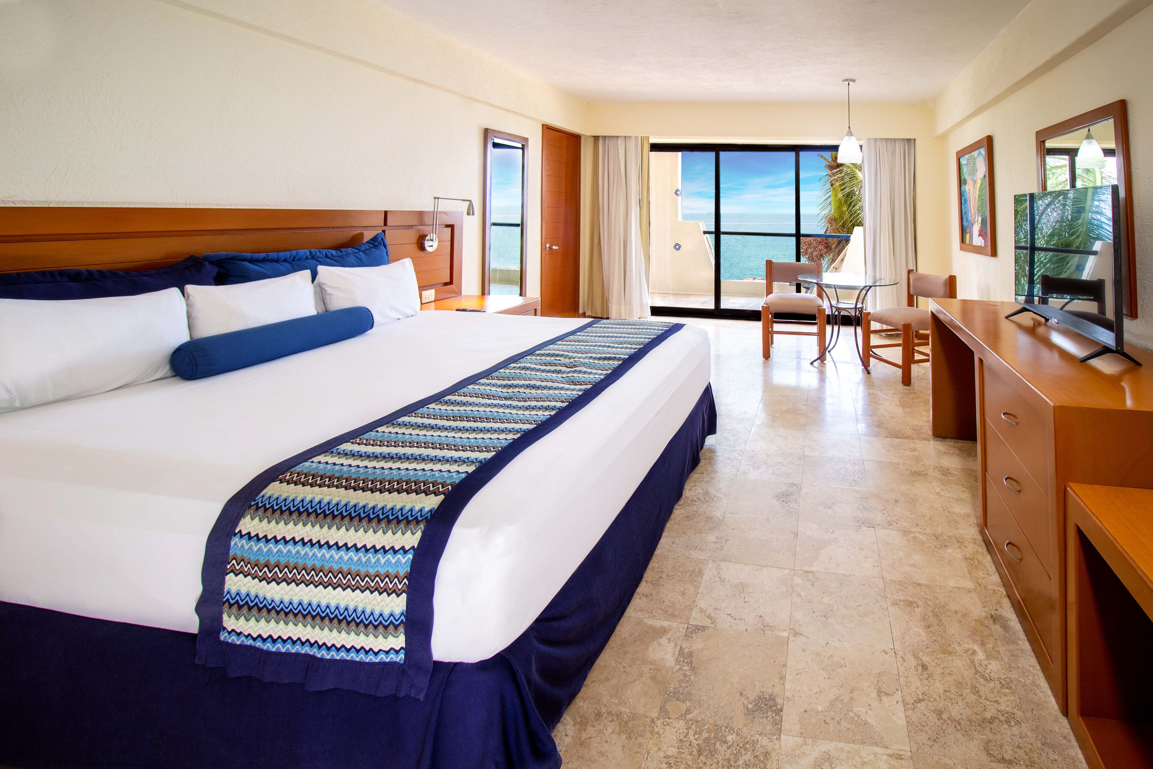 A hotel room with a large bed, a desk, and a view of the ocean.