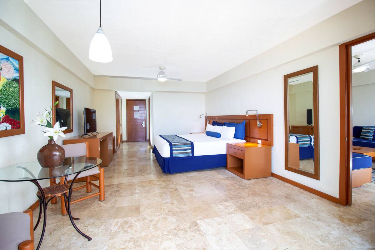 Una habitación de hotel con cama, escritorio, silla, televisor y espejo.
