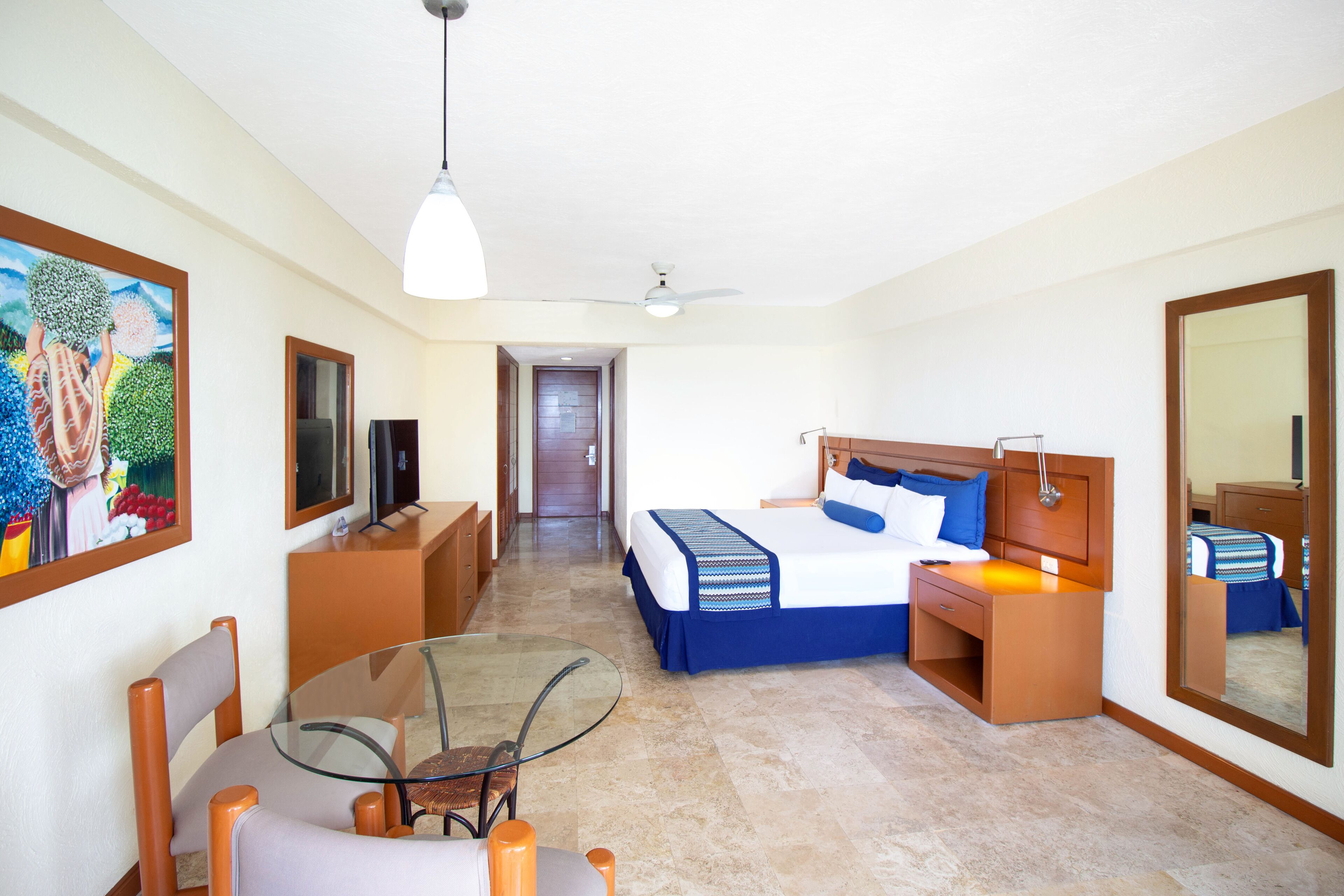 A hotel room with a bed, bedside table, lamp, and a glass table with chairs.