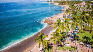 Un resort en la playa con piscina, palmeras y vista al océano.
