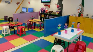 Children can play and learn in this vibrant playroom with play tables, a TV, bookshelf, and play structure.