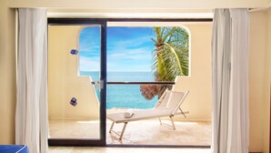 Una habitación con puerta de cristal corredera que da a un balcón con vistas al mar y palmeras.