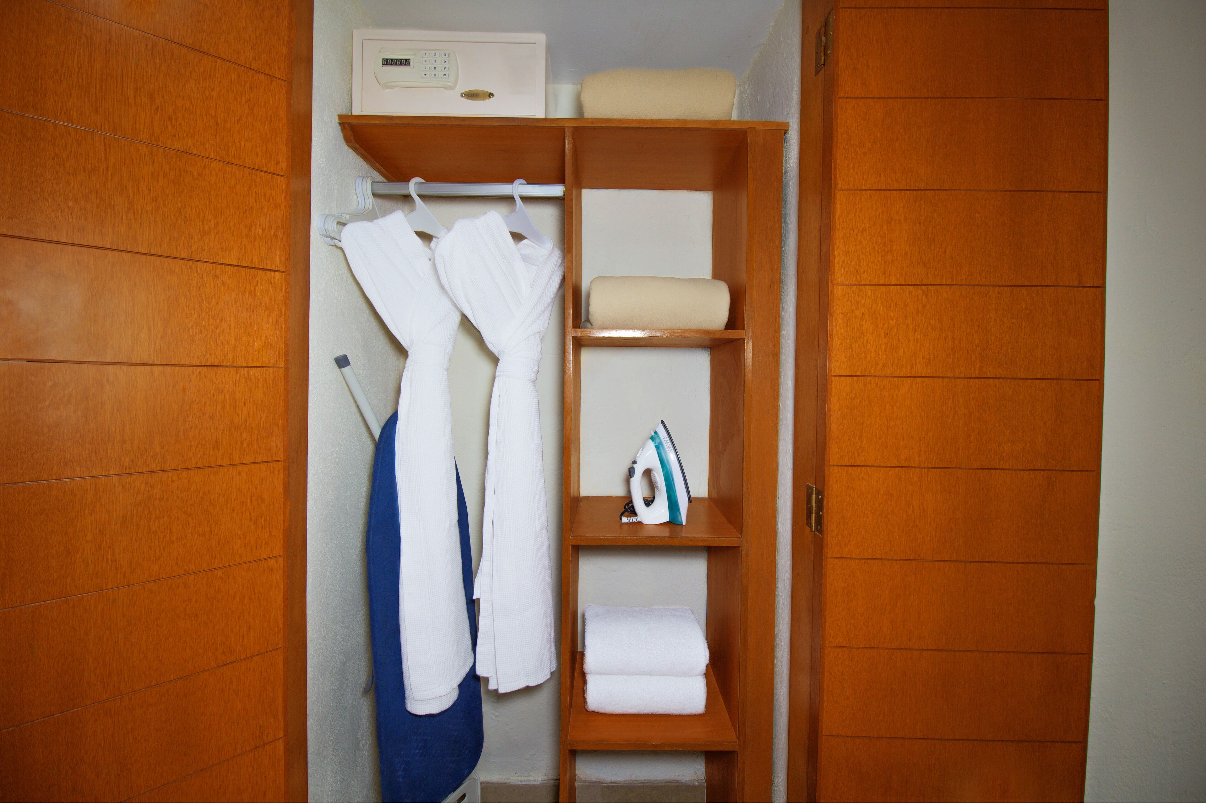 Une salle de bain avec des meubles en bois, un porte-serviettes et une étagère sur laquelle sont posés une serviette et un fer à repasser.