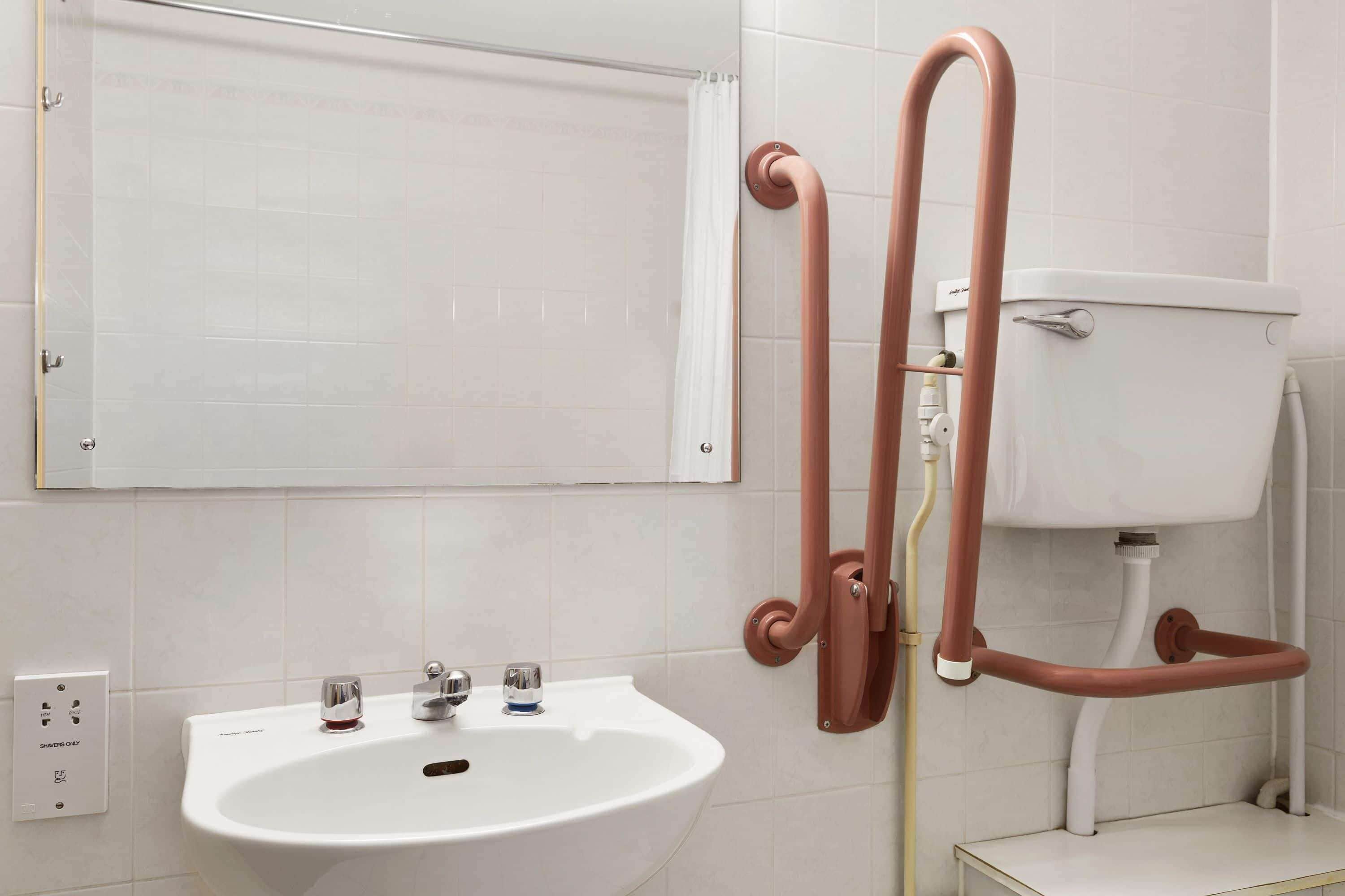 A bathroom with a white sink, two faucets, a mirror, and a toilet.