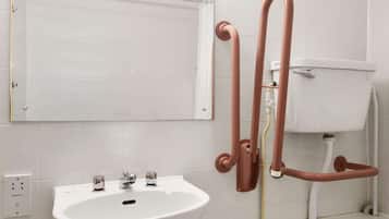 A bathroom with a white sink, two faucets, a mirror, and a toilet.
