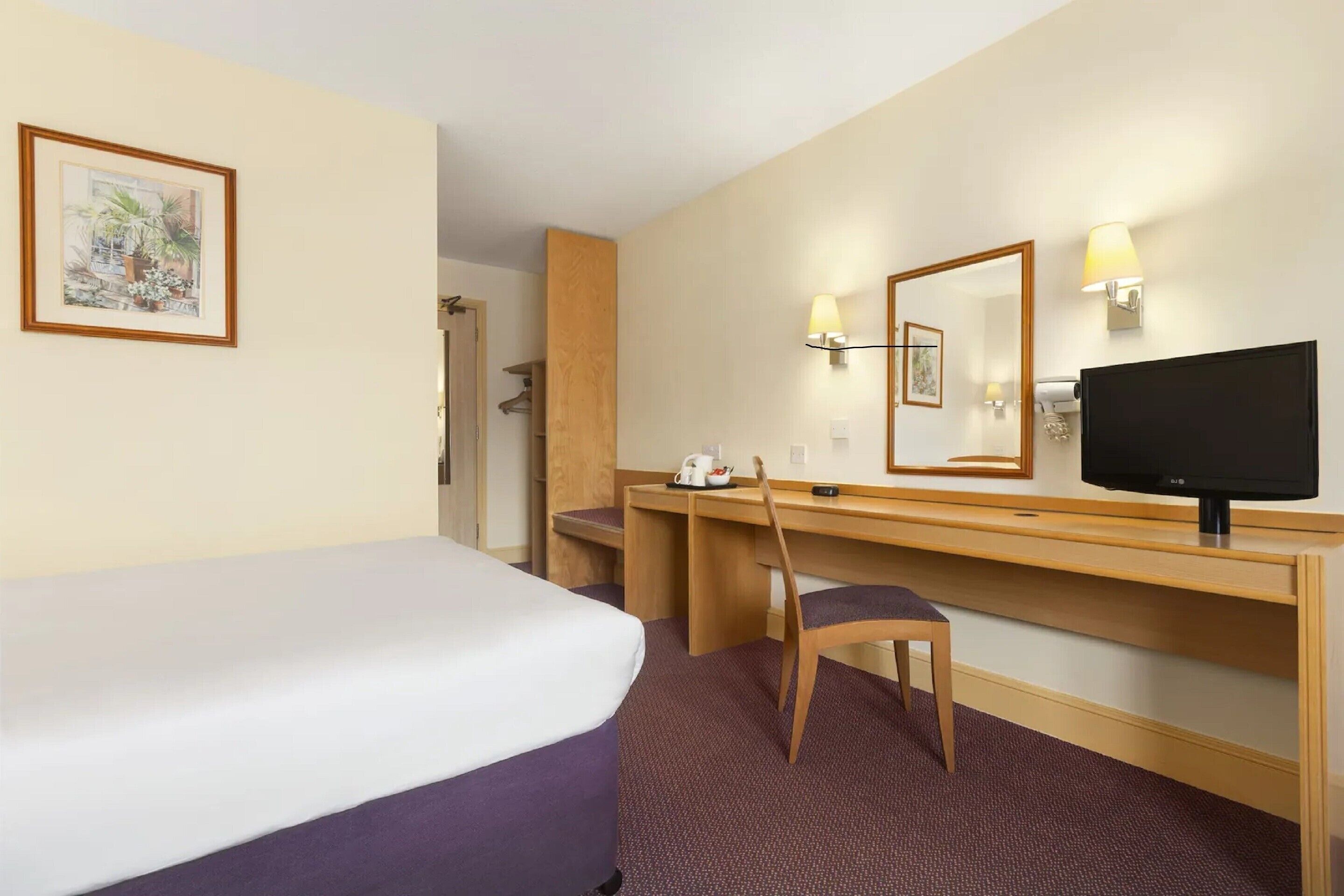 Ein Hotelzimmer mit Bett, Schreibtisch, Stuhl, Fernseher und Spiegel.