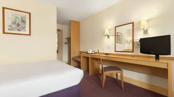 Ein Hotelzimmer mit Bett, Schreibtisch, Stuhl, Fernseher und Spiegel.