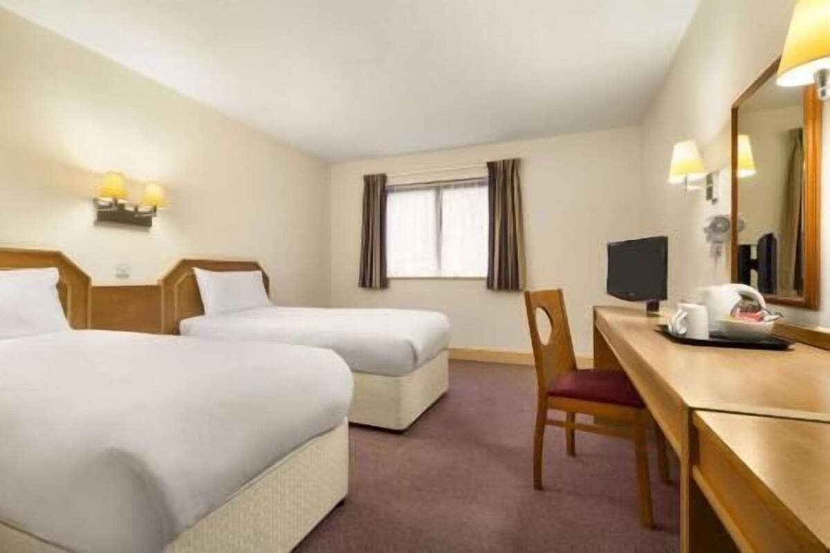 A hotel room with two beds, a desk with a chair, a television, and a window with curtains.