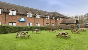 A Days Inn with a brick facade, multiple windows, and picnic tables in the front lawn. - Days Inn by Wyndham Sevenoaks Clacket Lane (Westerham)