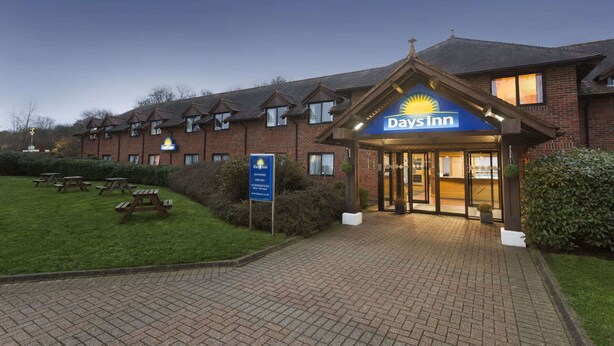 A Days Inn hotel entrance with a brick facade, a well-maintained lawn, and picnic tables. - Days Inn by Wyndham Sevenoaks Clacket Lane (Westerham)