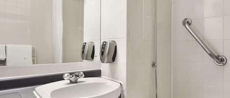 A modern bathroom with a white sink, a mirror, a glass shower enclosure, and a grab bar.