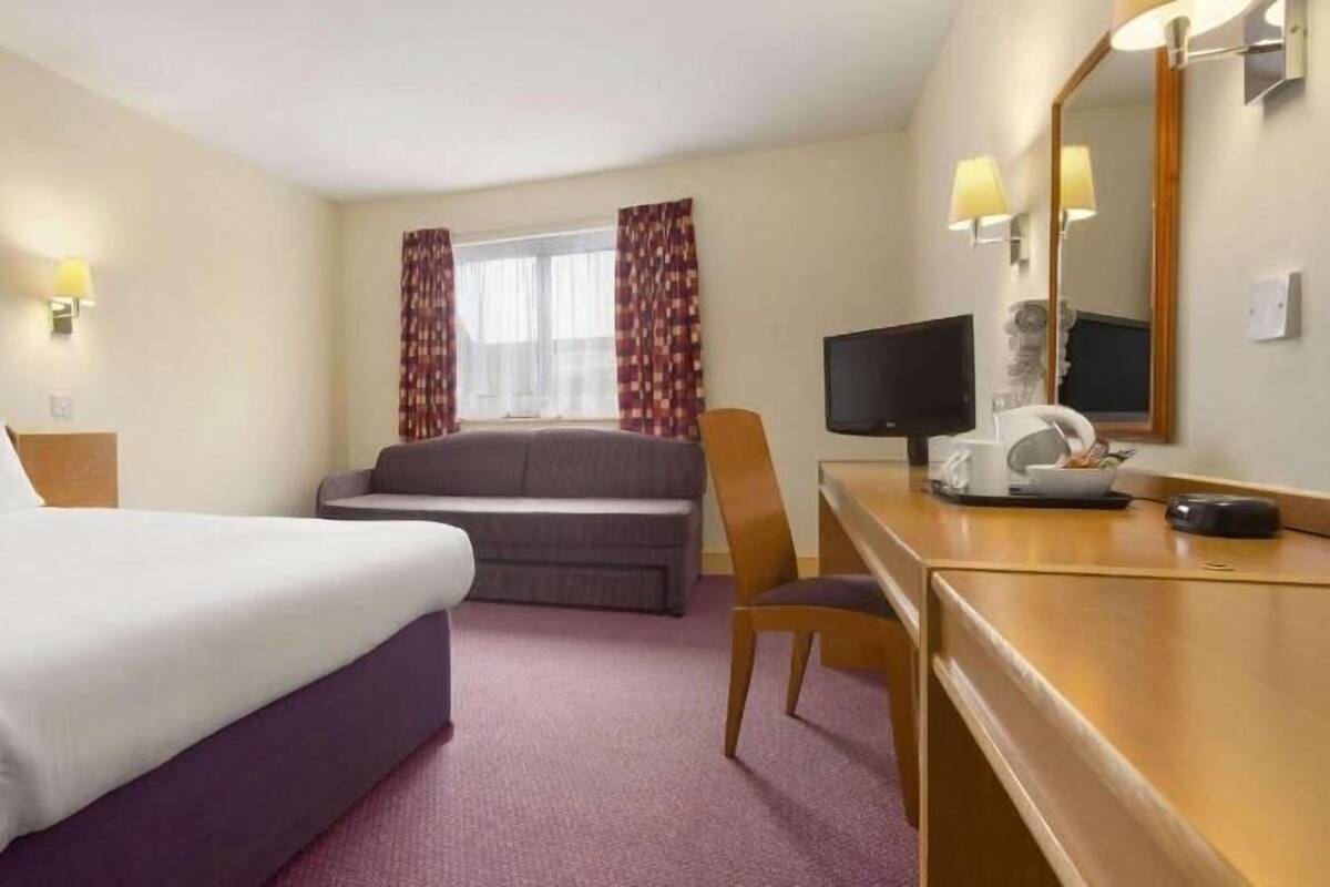 A hotel room with a bed, a sofa, a desk with a computer, and a TV.