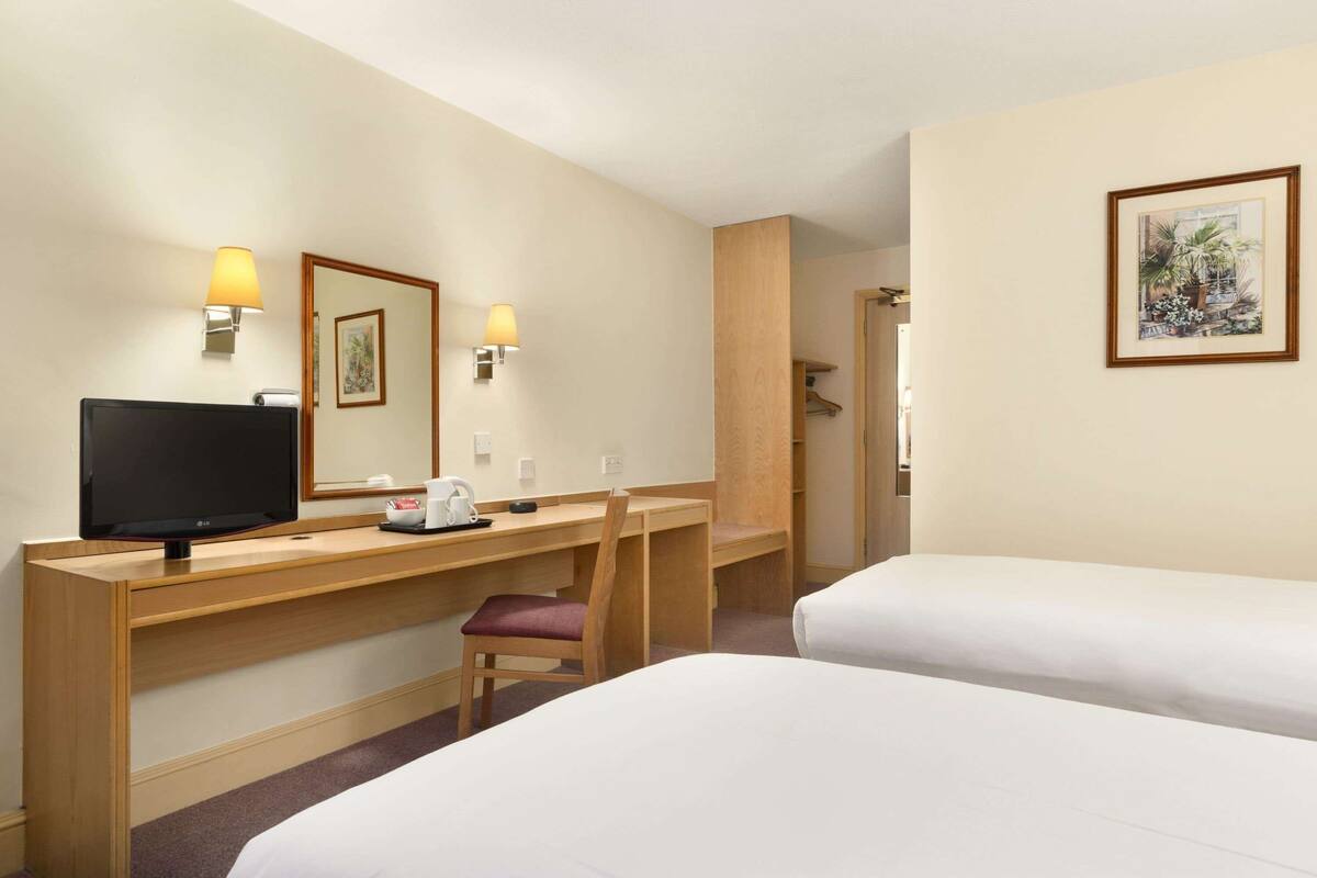 A hotel room with two beds, a desk with a television, a chair, and a mirror.