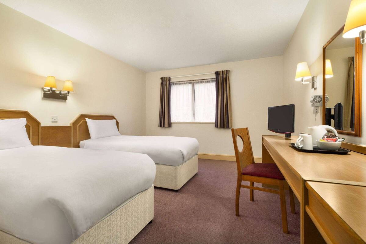 A hotel room with two beds, a desk with a chair, a television, and a window with curtains.