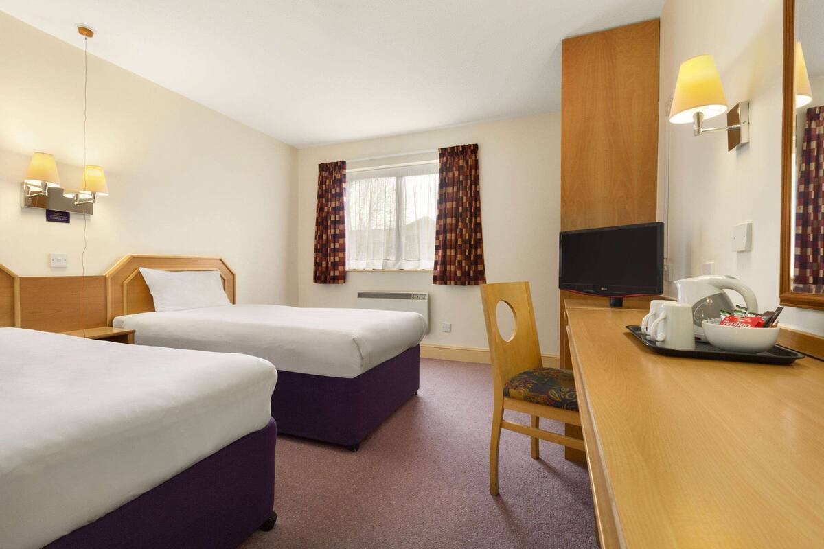 A hotel room with two beds, a desk with a chair, a television, and a window with curtains.