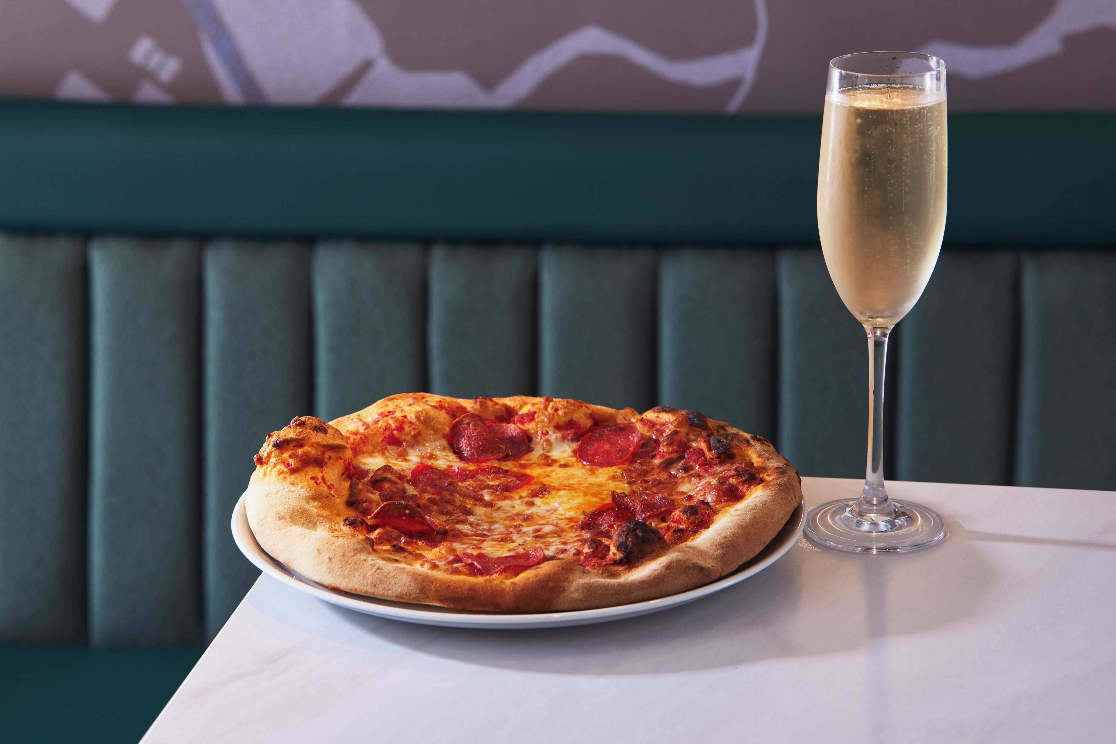 A pizza on a plate and a glass of champagne on a table.