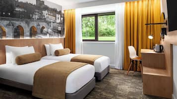 A hotel room with two beds, a desk, a chair, a window with curtains, and a mural on the wall.