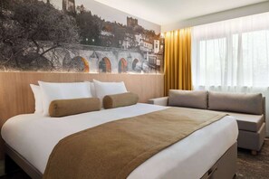 Ein Hotelzimmer mit einem großen Bett, einem Sofa, einem Wandgemälde einer Brücke und einem großen Fenster mit Vorhängen.