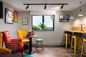 Relax in a spacious room with a large window offering a view of lush greenery, a seating area with a comfortable armchair, and a bar area with stools.