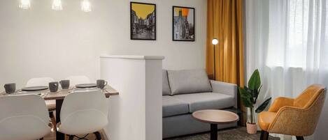 Een moderne hotelkamer met een zithoek, een bank, een ronde tafel en een groot raam met gordijnen.