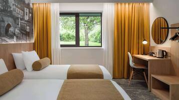 Une chambre d’hôtel avec deux lits, un bureau, une chaise, une grande fenêtre avec des rideaux et un miroir fixé au mur.