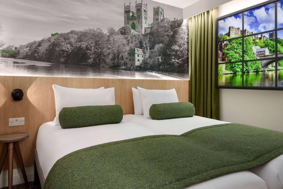 A hotel room with a bed, green pillows, a window with a view of a castle and river, and a curtain.