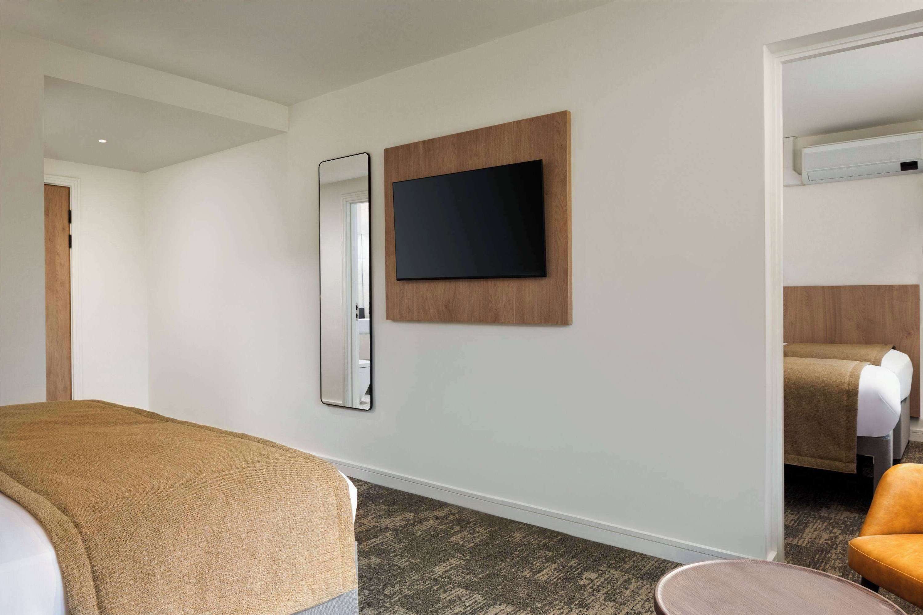 Quarto de hotel com uma cama, televisão na parede, espelho e uma pequena mesa redonda.