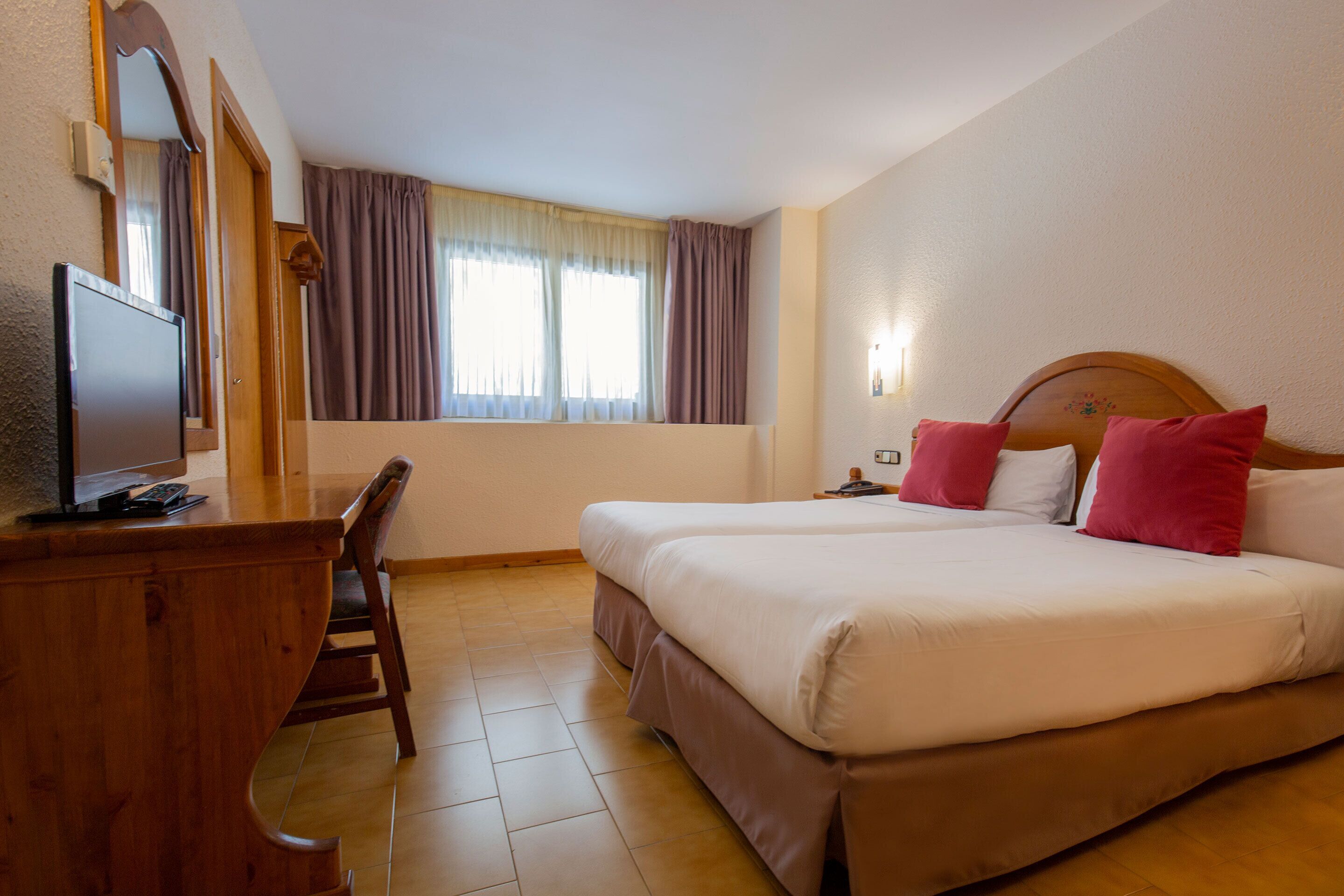 Ein Hotelzimmer mit Bett, Schreibtisch, Fernseher und einem Fenster mit Vorhängen.
