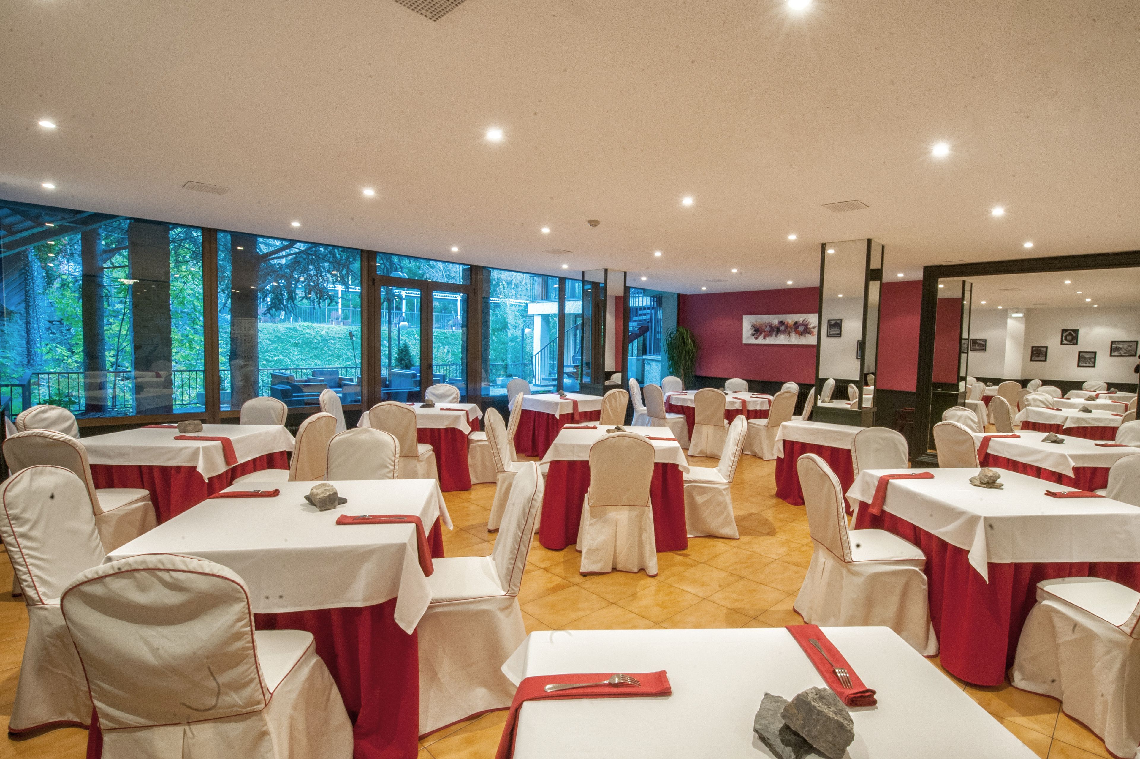 Uma sala de banquetes com mesas redondas, cadeiras brancas e toalhas vermelhas.