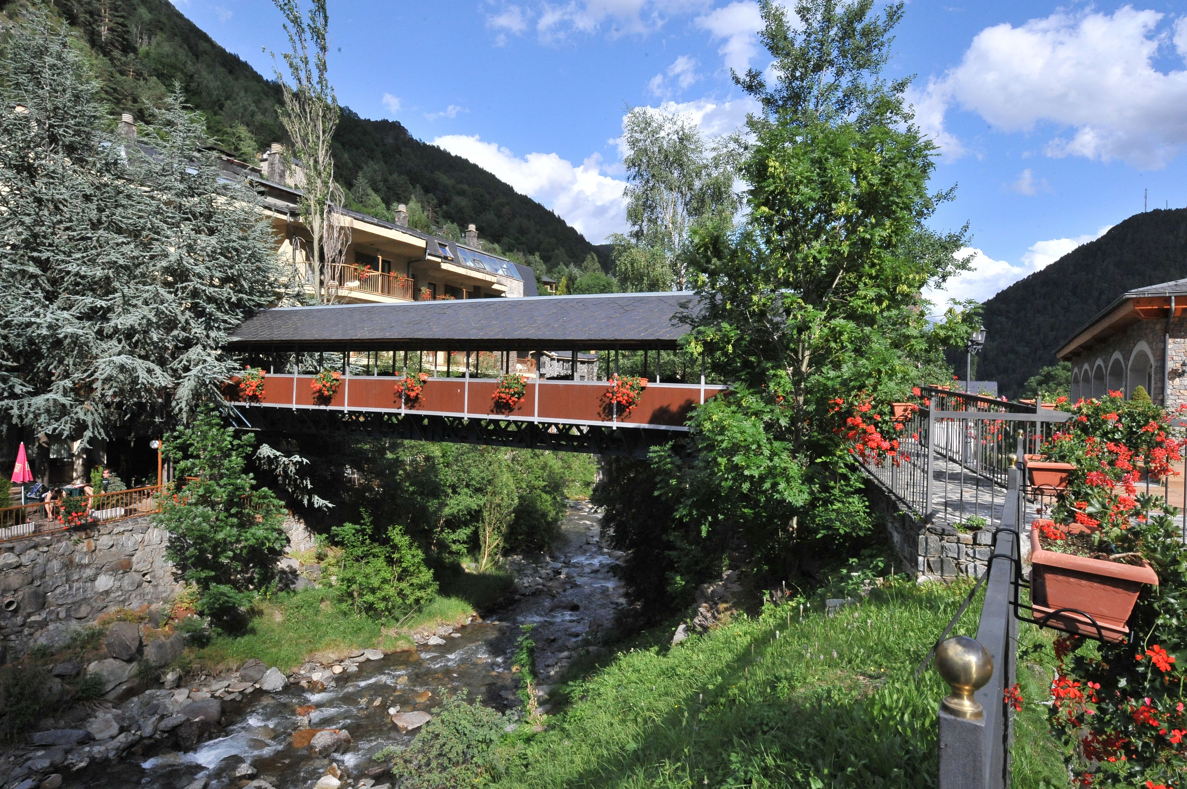 A bridge over a river with a building on the left and a building with red flowers on the right.