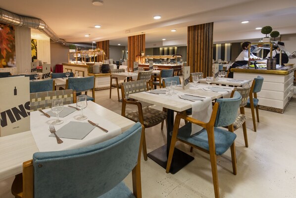 A restaurant with multiple tables set for dining, a bar area, and a kitchen in the background. - Hotel Sant Gothard by Nexta (Arinsal)