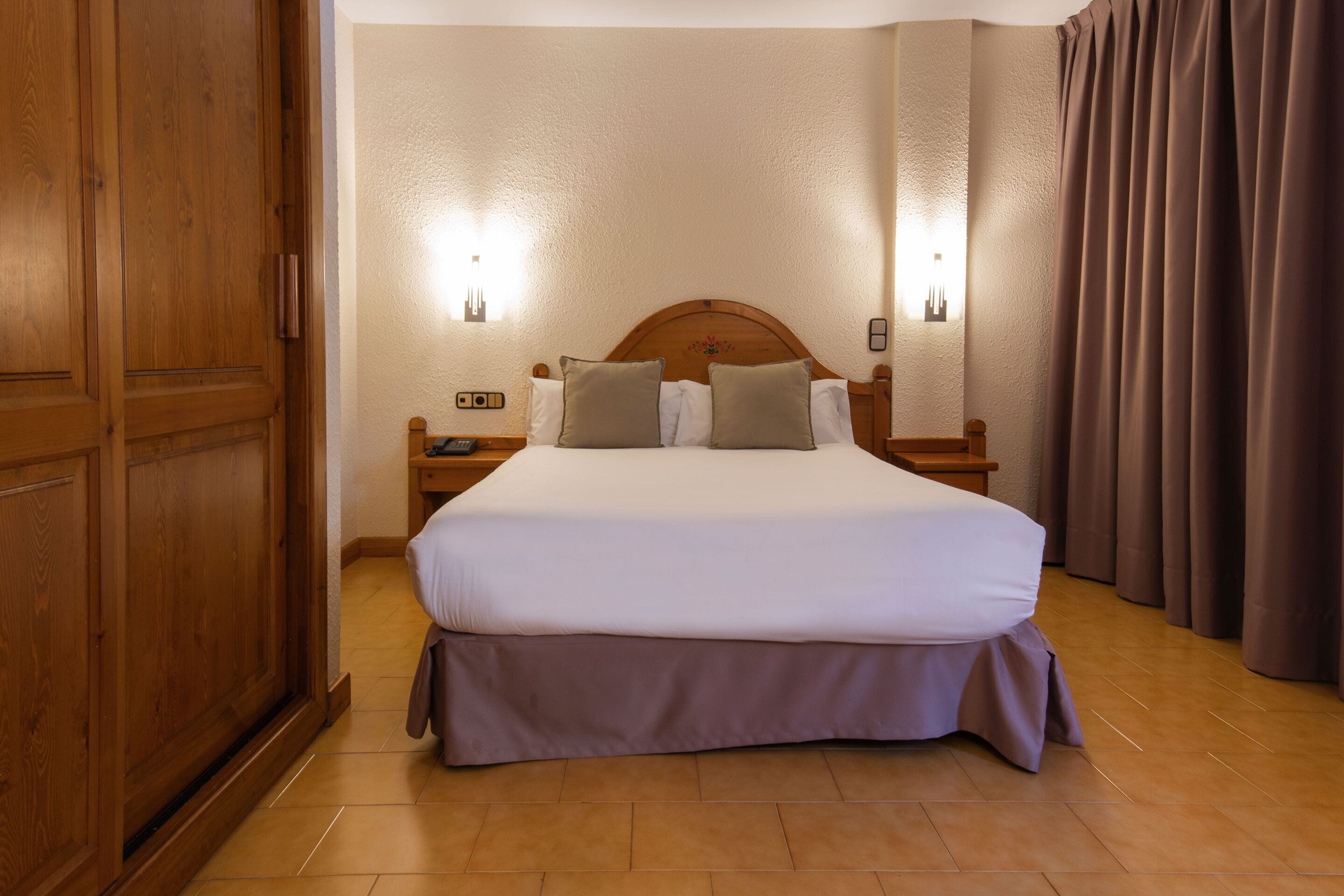 Een hotelkamer met een groot bed, een houten garderobe en twee nachtkastjes met lampen.