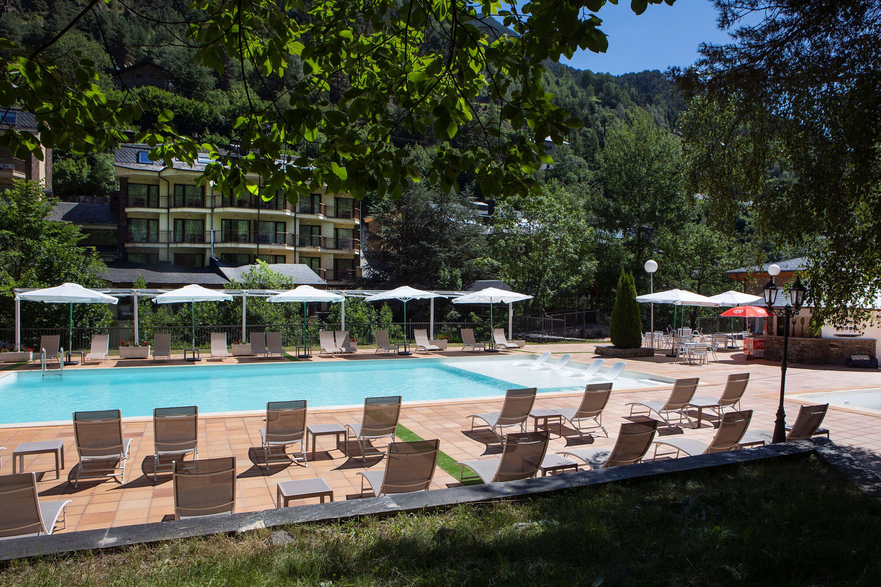 Ein Poolbereich mit Liegestühlen und Sonnenschirmen, umgeben von Bäumen und Gebäuden.
