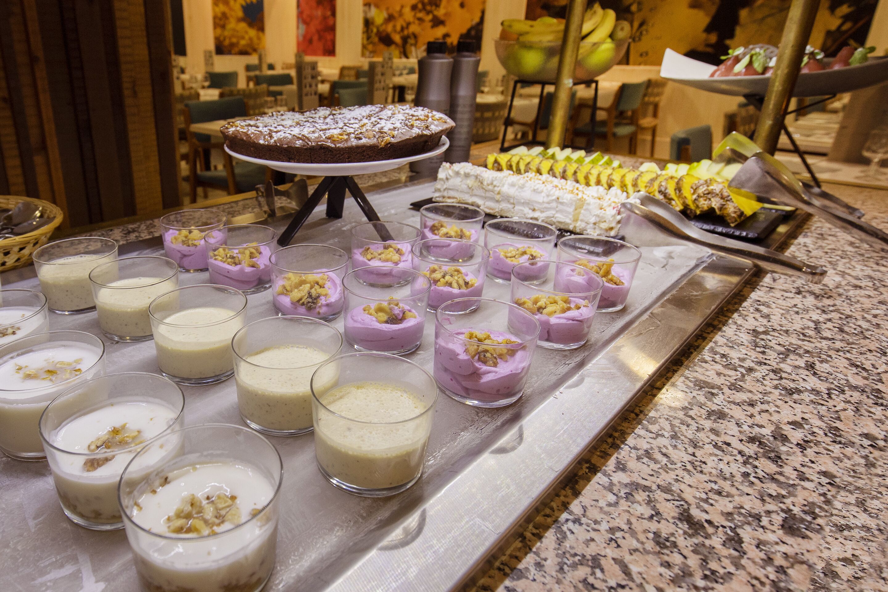 A buffet with various desserts including a chocolate cake, fruit skewers, and small dessert cups.