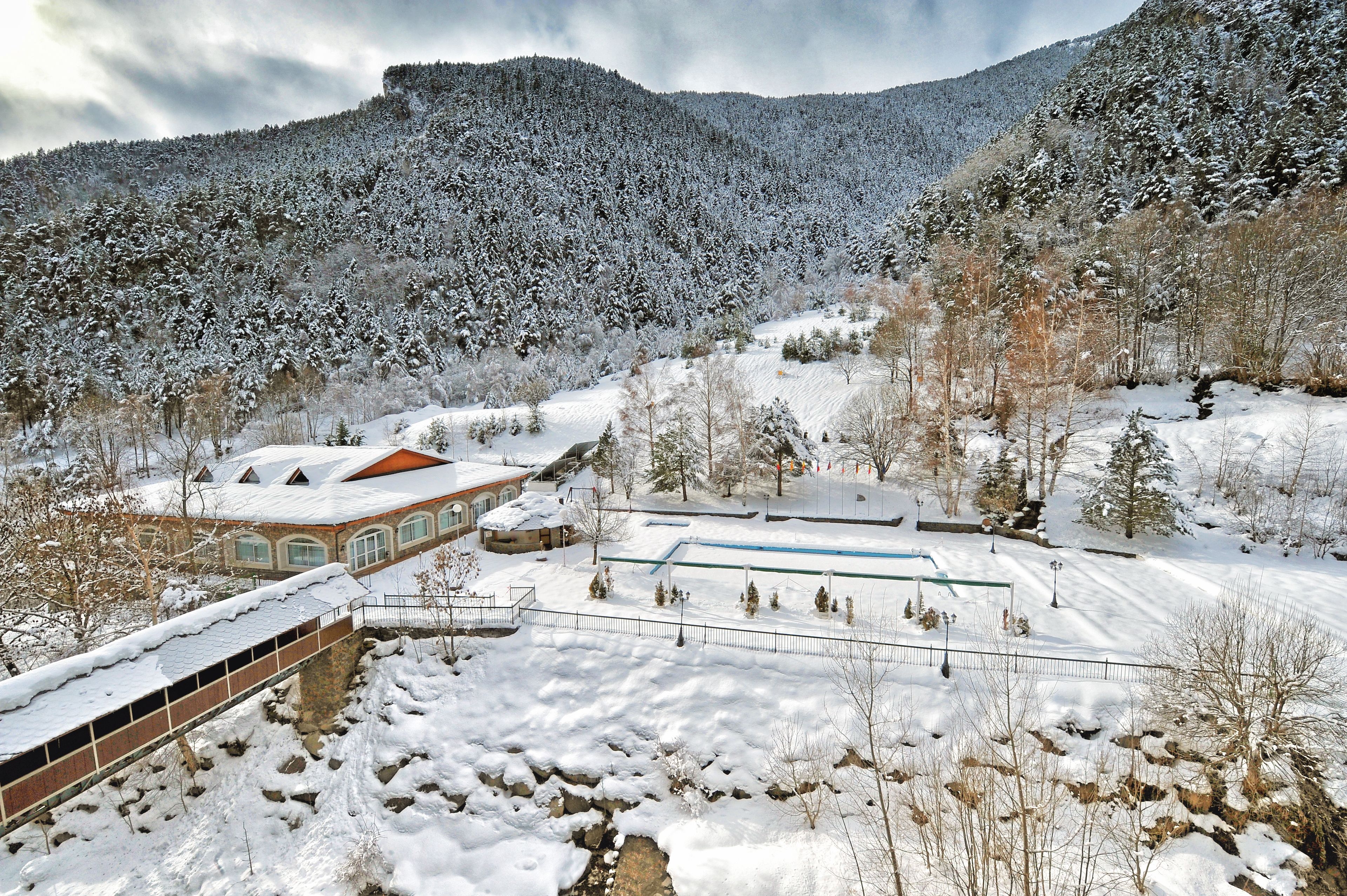 A snow-covered landscape with a building featuring a red roof and a bridge.