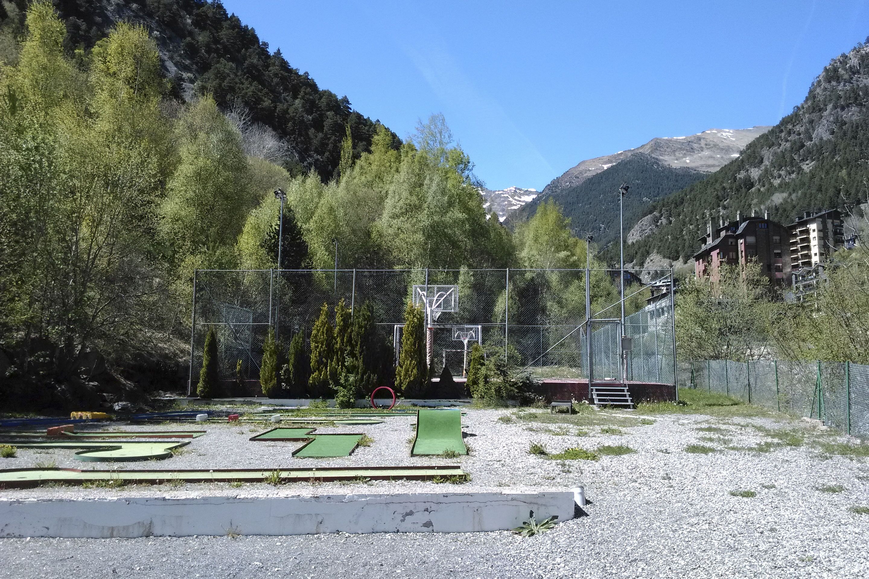 Un terrain de golf entouré d’une clôture en filet, avec un panier de basket et un bâtiment visible au loin.