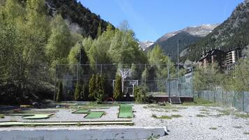 Ein Golfplatz mit einem Netzzaun, einem Basketballkorb und einem Gebäude im Hintergrund.