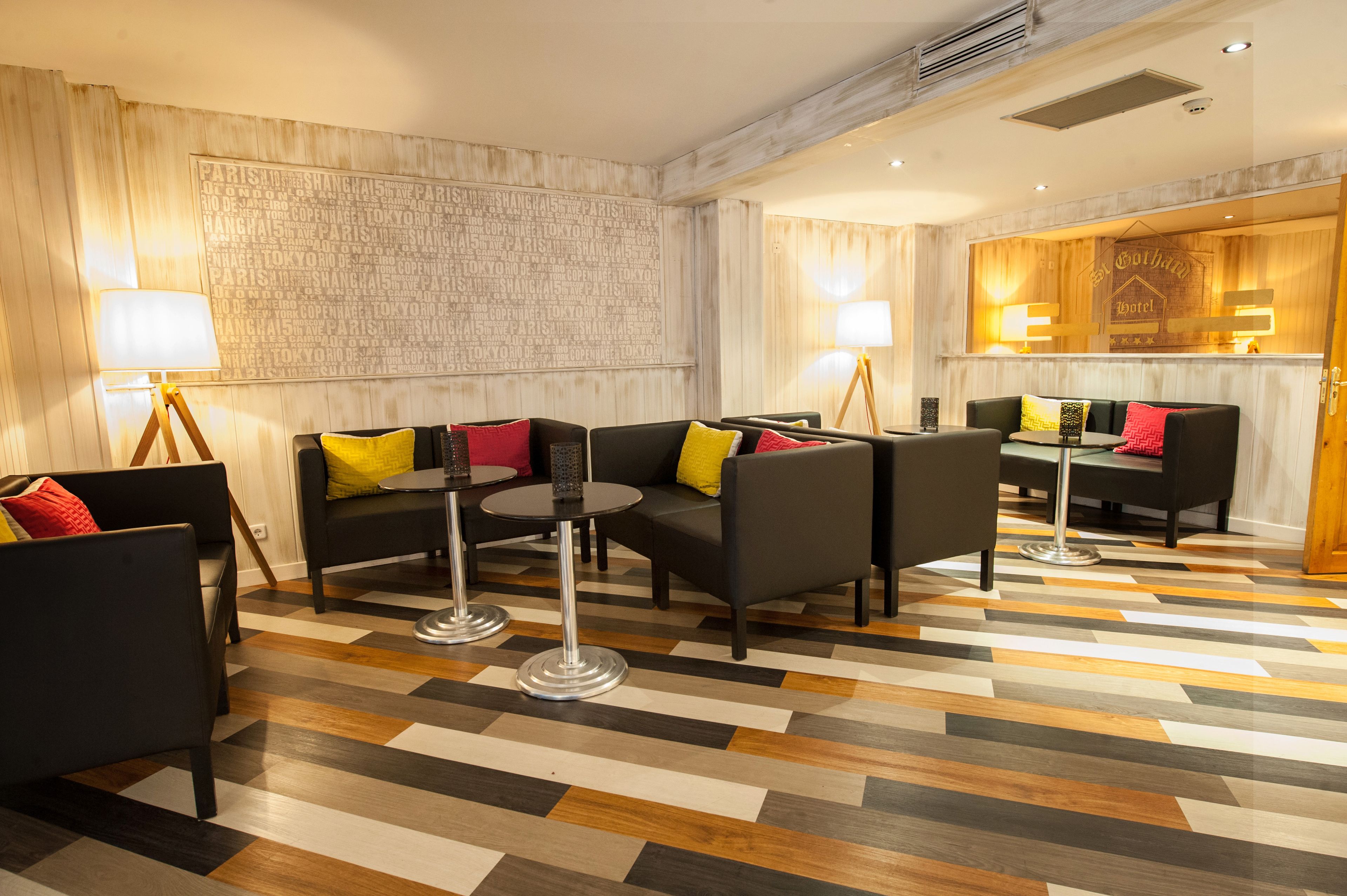 Eine Hotelhalle mit modernem Design, mit einem Schachbrettmuster-Boden, schwarzen Sofas mit bunten Kissen und einem hölzernen Empfangstresen.