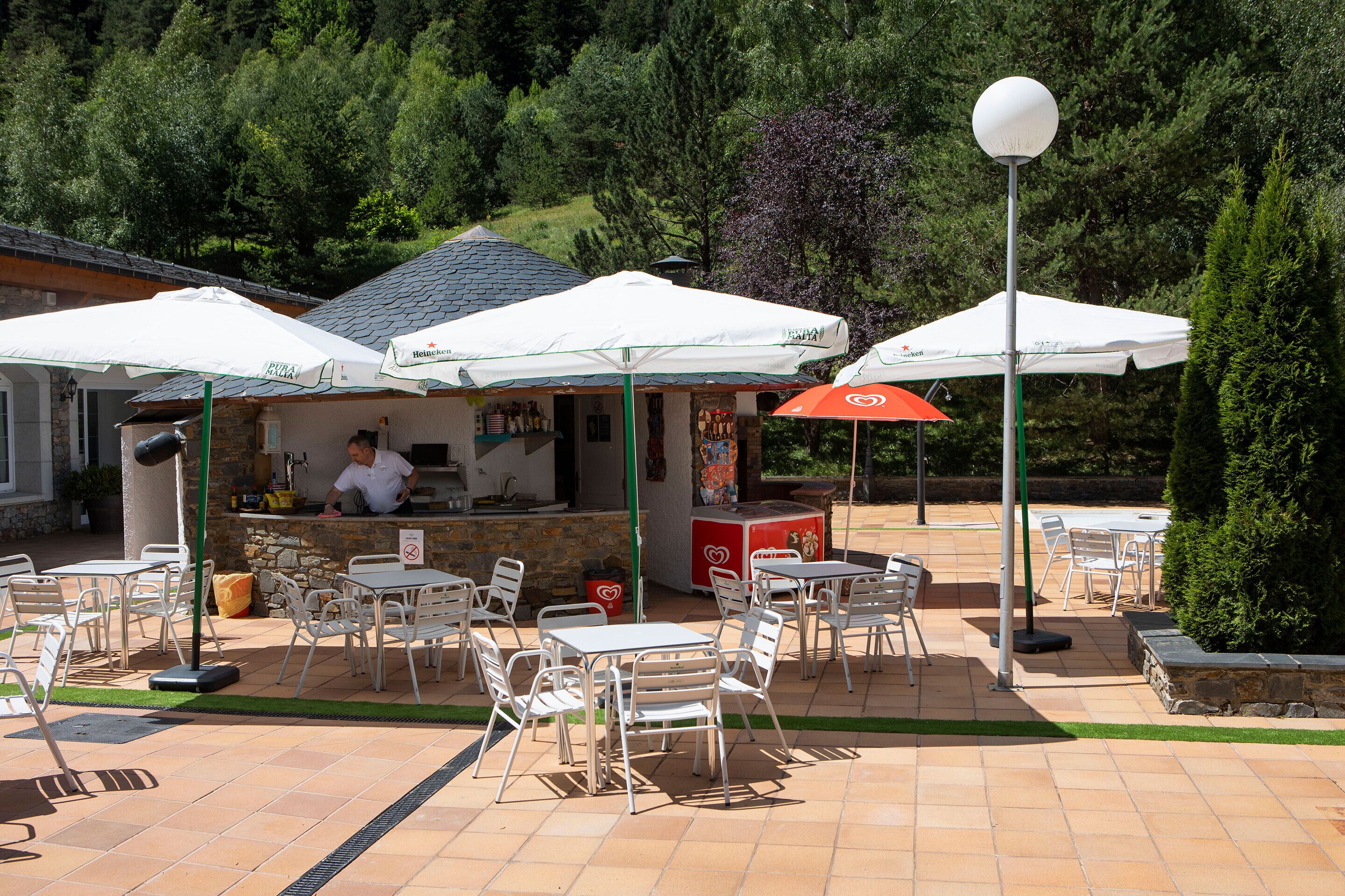 An outdoor café with white tables and chairs, covered by white umbrellas, and a red umbrella.