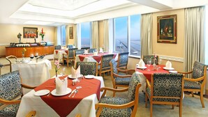 Ein Hotel-Speisesaal mit mehreren gedeckten Tischen, großen Fenstern mit Blick und einer Bar.