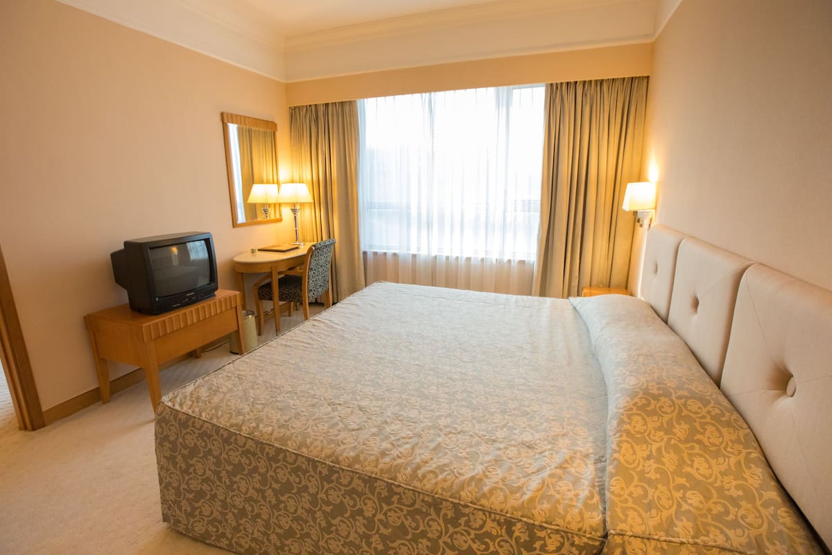 A hotel room with a large bed, a desk with a television, a chair, and a window with curtains.