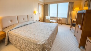 Ein Hotelzimmer mit einem großen Bett, einem Schreibtisch, einem Sessel und Blick aufs Meer.