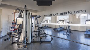 A gym with various exercise machines, a mirrored wall, and a view of the city through large windows. - Monreale Express Ribeirão Preto (Ribeirão Preto)