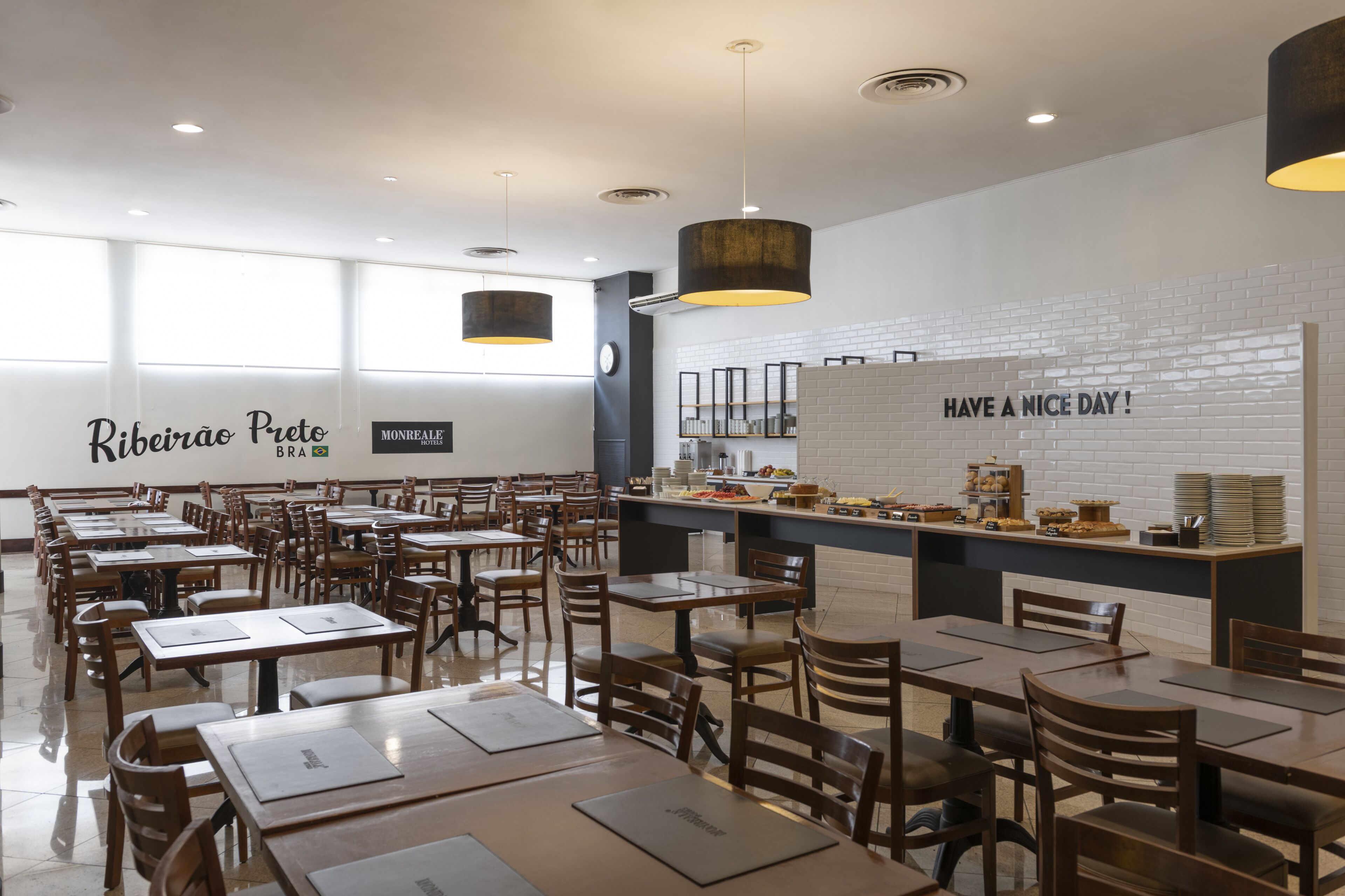 A restaurant with a long counter, wooden tables, and chairs. There is a sign that says "Have a nice day!" and another that says "Ribeirão Preto".