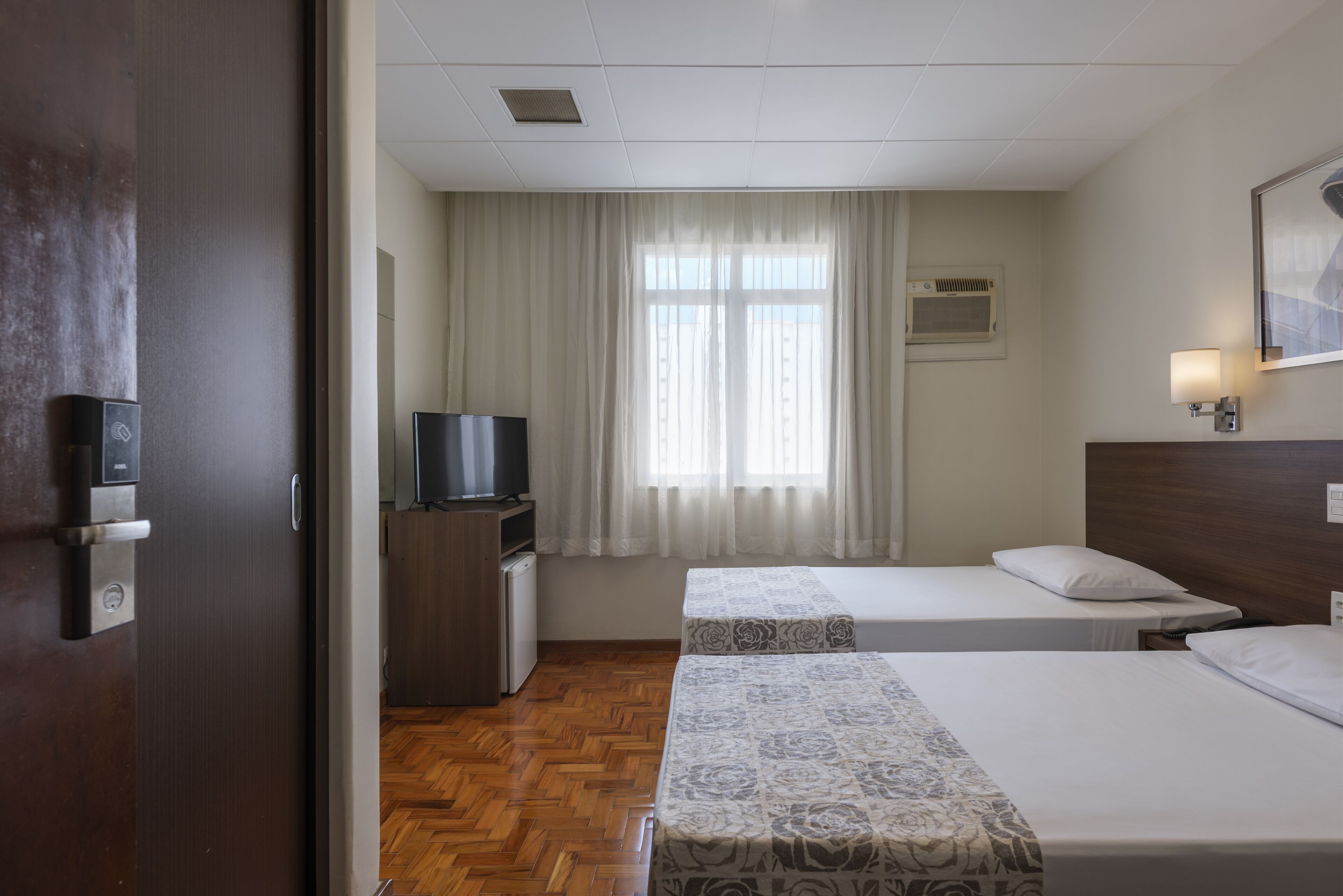 Een hotelkamer met twee bedden, een televisie, een bureau en een raam met gordijnen.