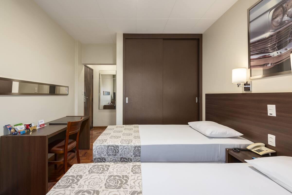 Ein Hotelzimmer mit Schreibtisch, zwei Betten, einem Sessel, einem Telefon und einer Lampe.
