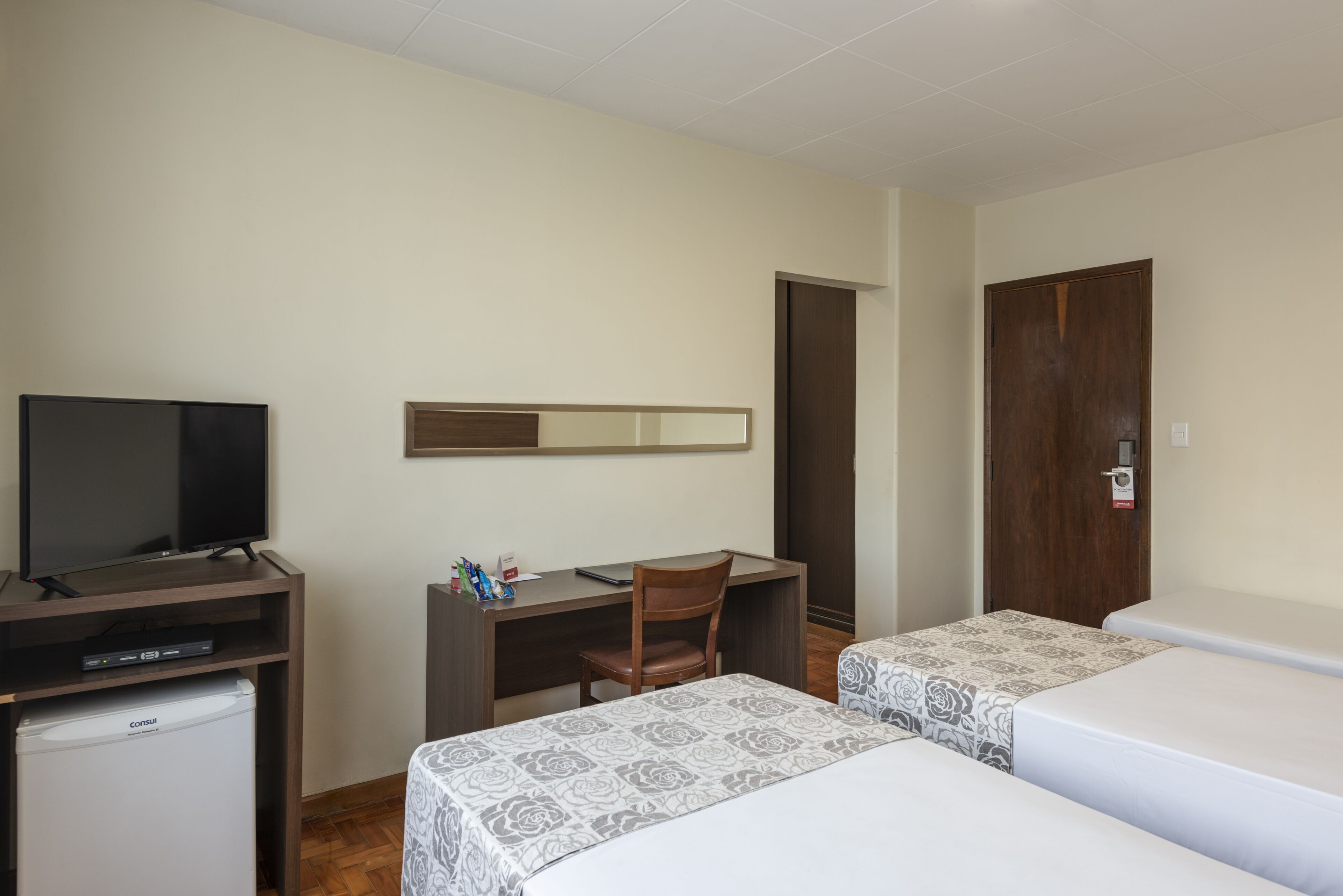 Hotellihuone, jossa on televisio, työpöytä, tuoli, kaksi sänkyä ja vaatekaappi.