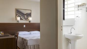 A hotel room with a bed, a desk, a chair, a painting on the wall, a sink, and a mirror.