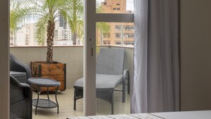 A hotel room with a bed, a balcony with a palm tree, and a view of buildings. - Monreale Express Ribeirão Preto (Ribeirão Preto)